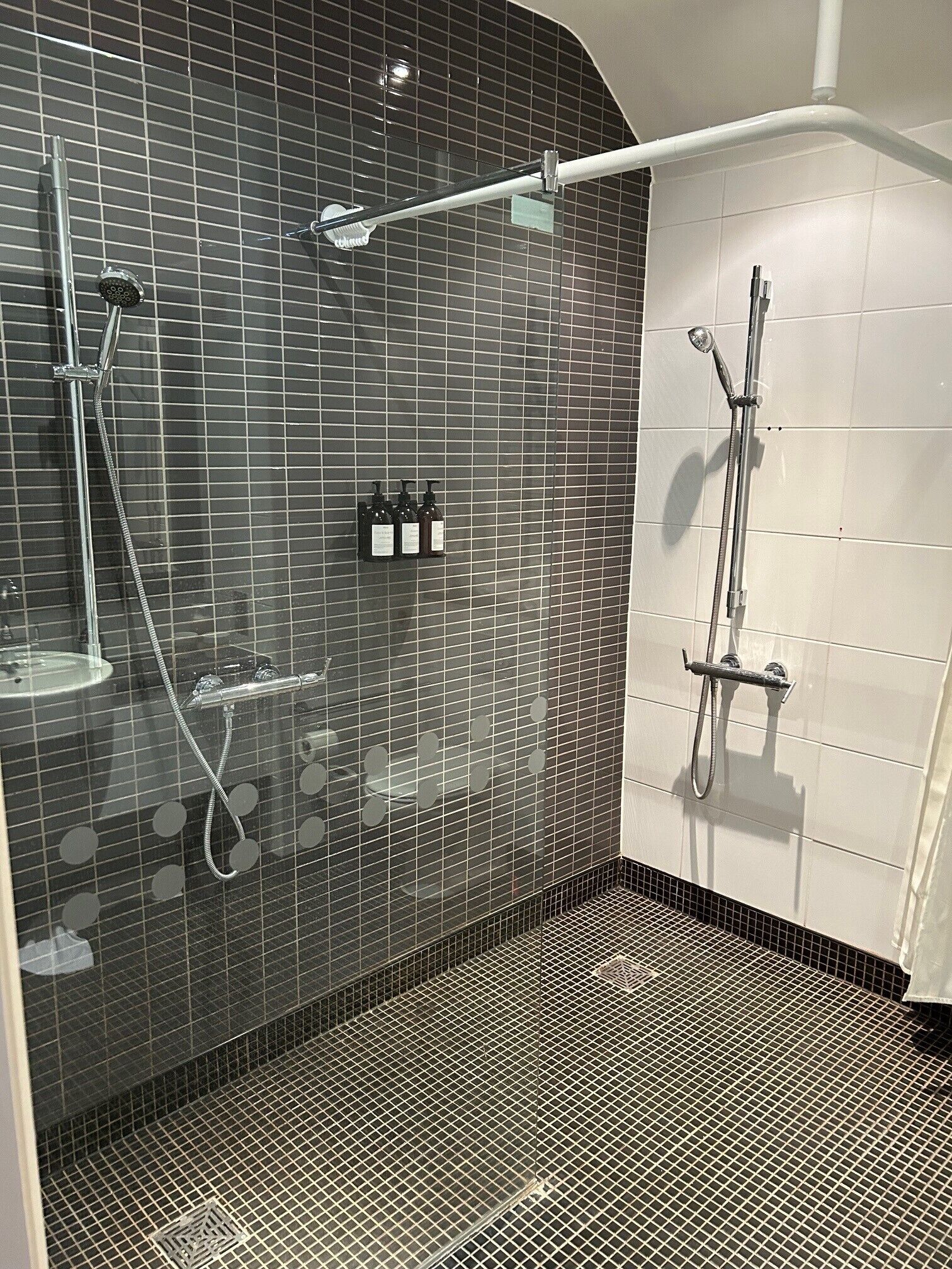 A modern bathroom with a glass shower enclosure, a handheld showerhead, and a wall-mounted faucet.