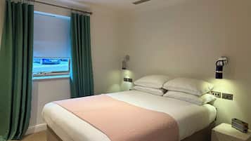 Un dormitorio con cama, cortinas, una mesita de noche y una lámpara de pared.