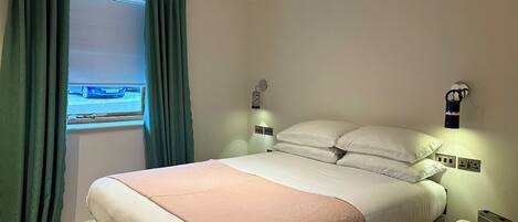 A bedroom with a bed, curtains, a bedside table, and a wall-mounted light.