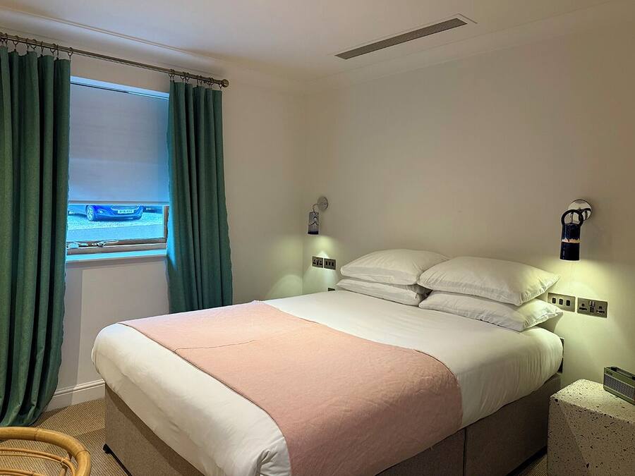 Un dormitorio con cama, cortinas, una mesita de noche y una lámpara de pared.