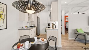 A modern kitchen with white cabinets, a dining area with a black table and chairs, and a living area with a gray sofa. - DreamCatcher-N Walk to Shop/Dine/Hike (Sedona)