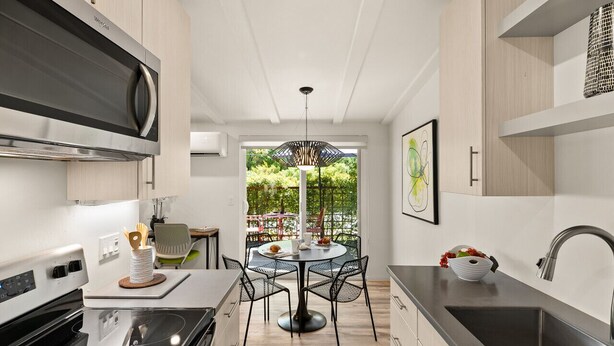 A modern kitchen with a built-in stove, a dining area with a round table and chairs, and a view of a garden through a large window. - DreamCatcher-N Walk to Shop/Dine/Hike (Sedona)