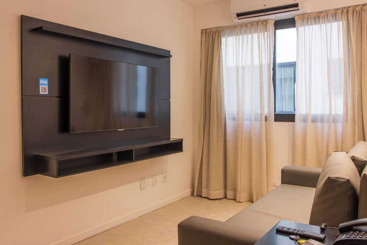 A modern living room with a flat-screen TV mounted on the wall, a sofa, and a coffee table with remote controls.