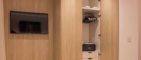 A bedroom with a bed, a TV mounted on the wall, a wooden wardrobe, and a bedside table.
