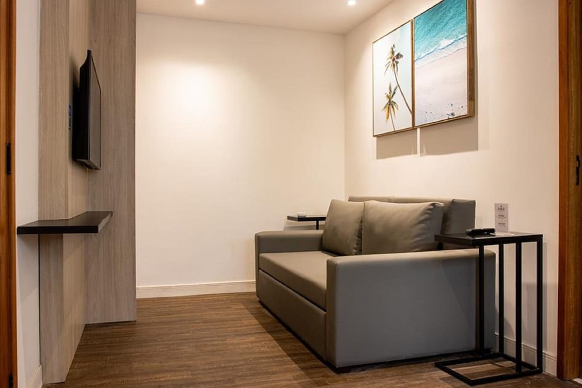 Uma sala de estar moderna com um sofá cinzento, uma TV na parede e um quadro de uma praia.