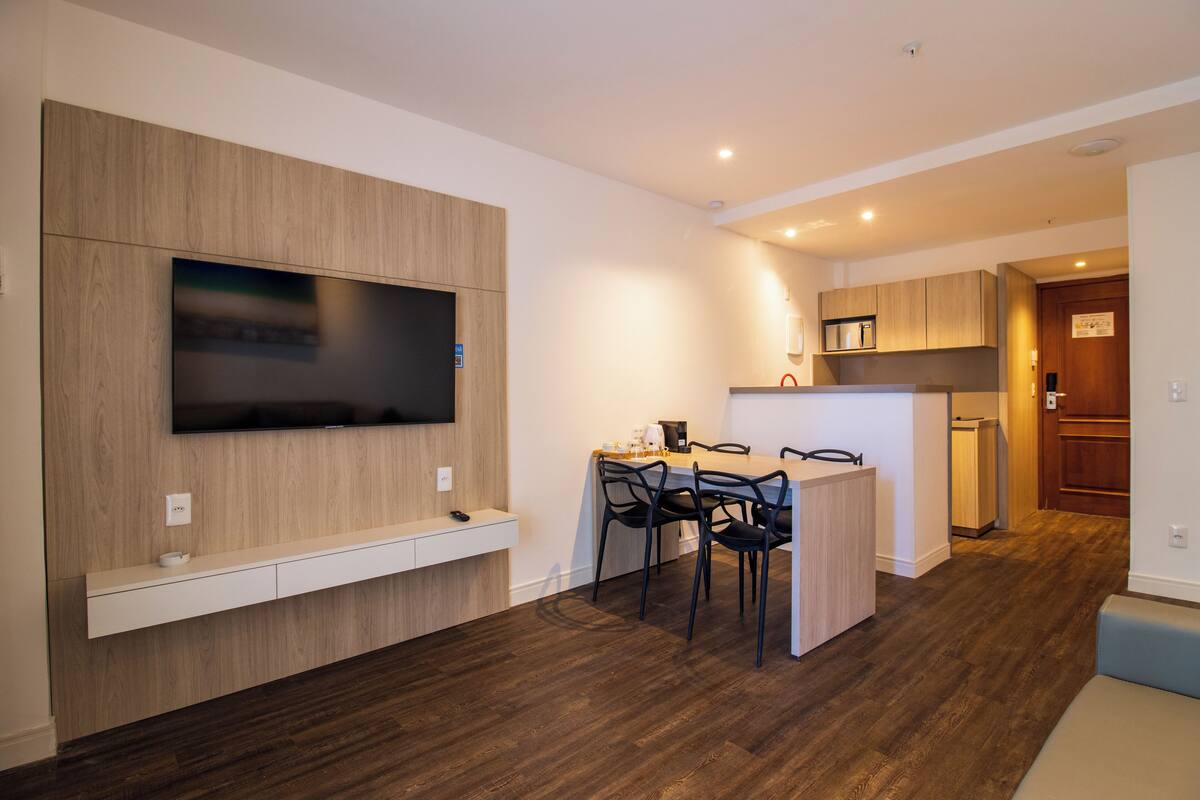 A modern kitchen with a built-in TV, wooden cabinetry, and a dining area with chairs.