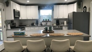 Een moderne keuken met witte kasten, een centraal eiland met barstoelen, een magnetron, fornuis en een koelkast.