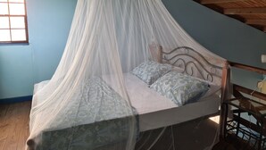 A bed with a canopy in a room with a sloped ceiling and a window. - BLUE COTTAGE Almost Paradise (Sauteurs)
