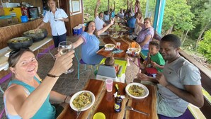 A group of people dining at a wooden table with a view of greenery outside. - FISH COTTAGE Almost Paradise (Sauteurs)
