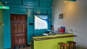 A small kitchen with a green counter, a sink, and two wooden stools. - FISH COTTAGE Almost Paradise (Sauteurs)