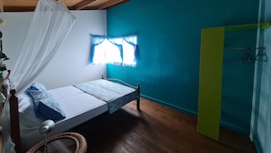 A single bed with a mosquito net, a window with blue curtains, and a wooden ceiling. - FISH COTTAGE Almost Paradise (Sauteurs)