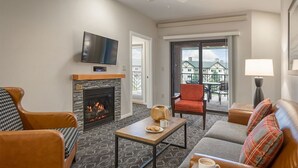 A living room with a fireplace, a television mounted above it, and a balcony with outdoor seating.