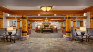 A lobby with stone flooring, wooden pillars, and a central seating area with chairs and a table.