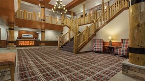 A spacious lobby with a checkered carpet, wooden staircase, and a reception desk.