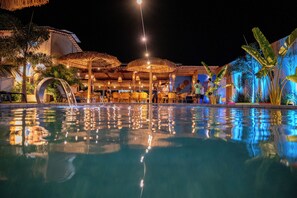 A nighttime pool area with clear water reflecting lights, surrounded by palm trees and umbrellas. - Pousada Solarium de Gostoso (São Miguel do Gostoso)