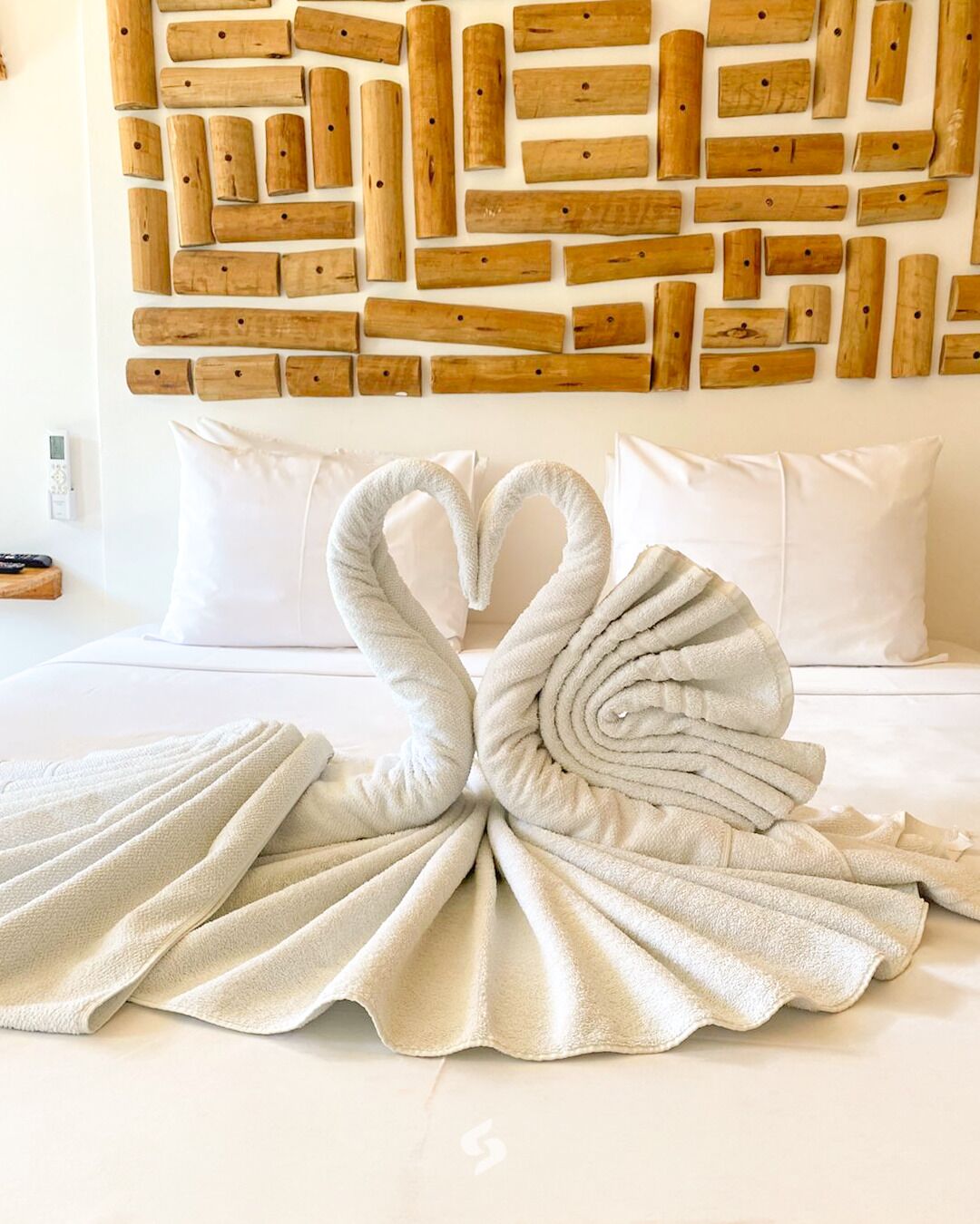 Habitación de hotel con cama, almohadas, una obra de arte de madera montada en la pared y una toalla doblada en forma de cisne.