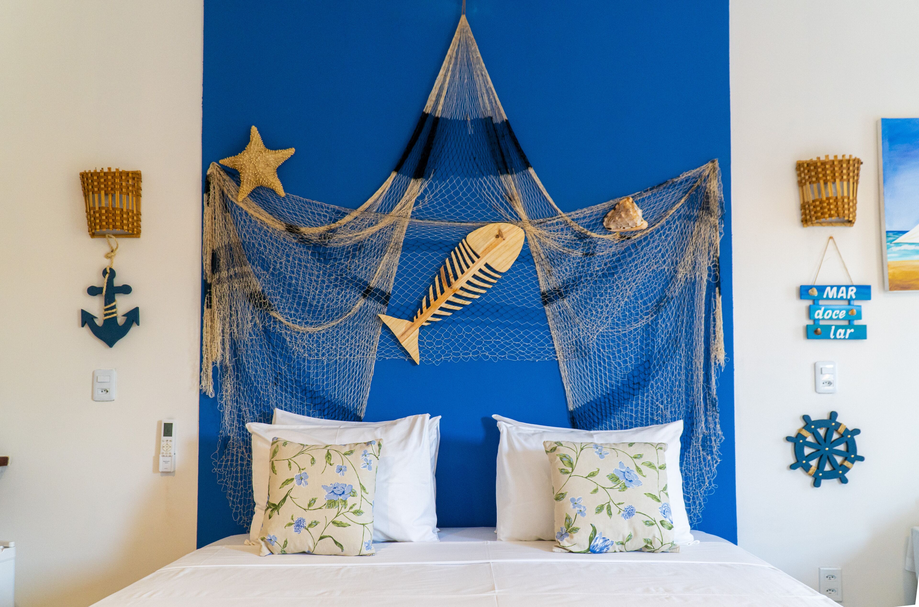Une chambre avec un lit, un mur bleu et des éléments de décoration sur le thème de la mer, notamment une étoile de mer, des poissons et un filet.