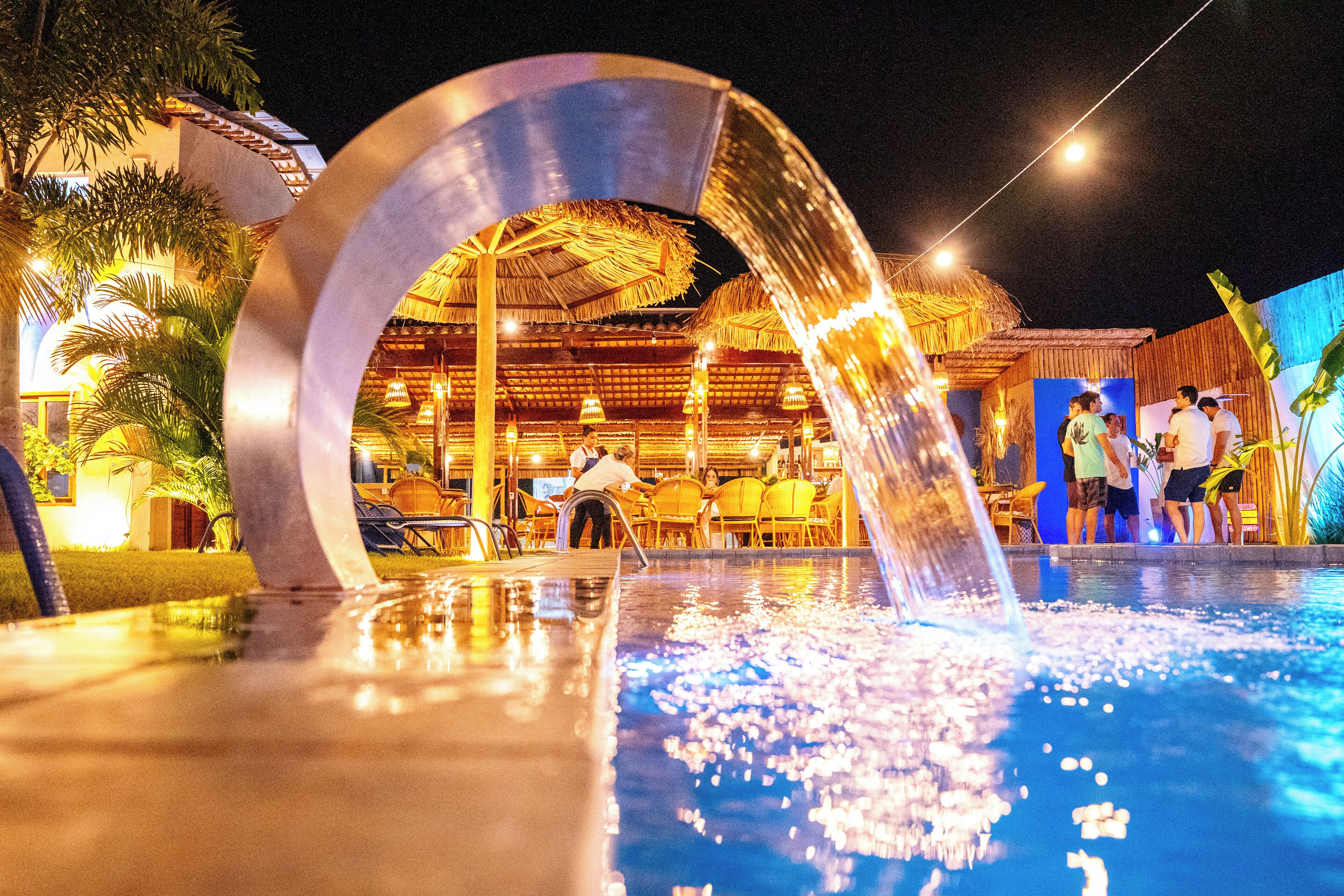 A pool area with a water feature, outdoor seating, and a thatched-roof structure.
