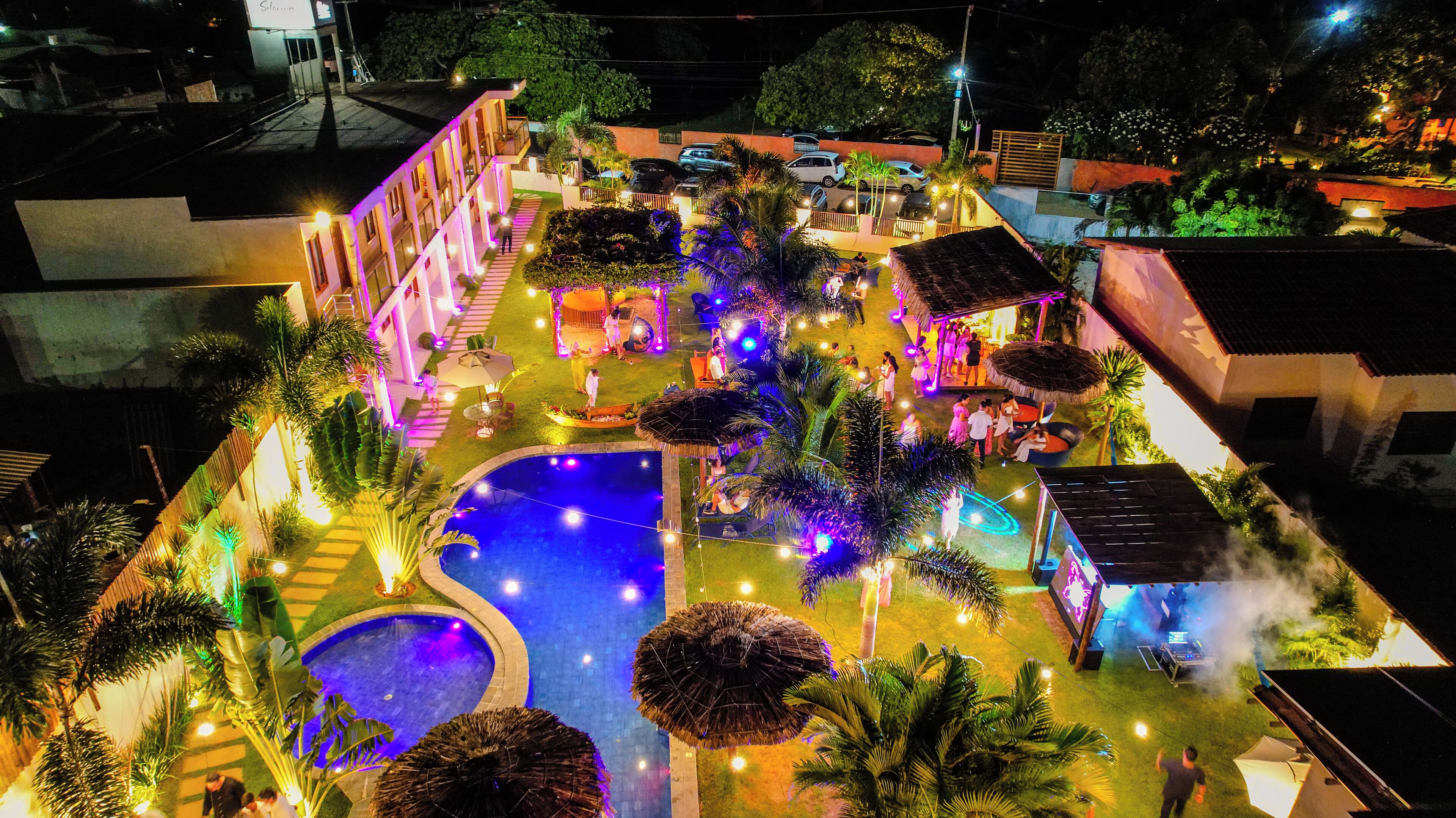 Un área de piscina con una piscina central grande y una piscina más pequeña contigua, rodeada de palmeras y zonas de estar al aire libre.