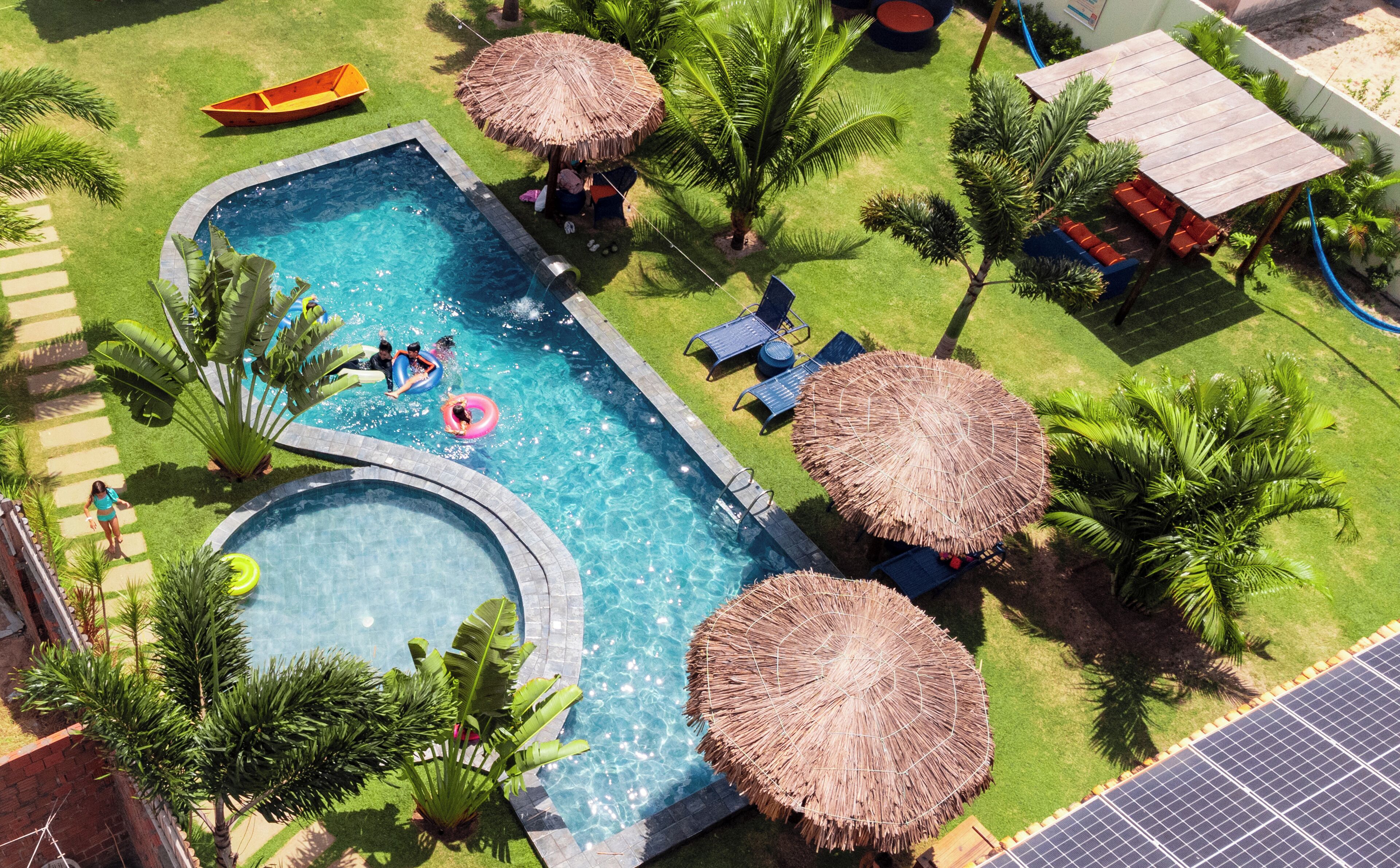 A swimming pool with a curved edge, surrounded by palm trees and thatched umbrellas.