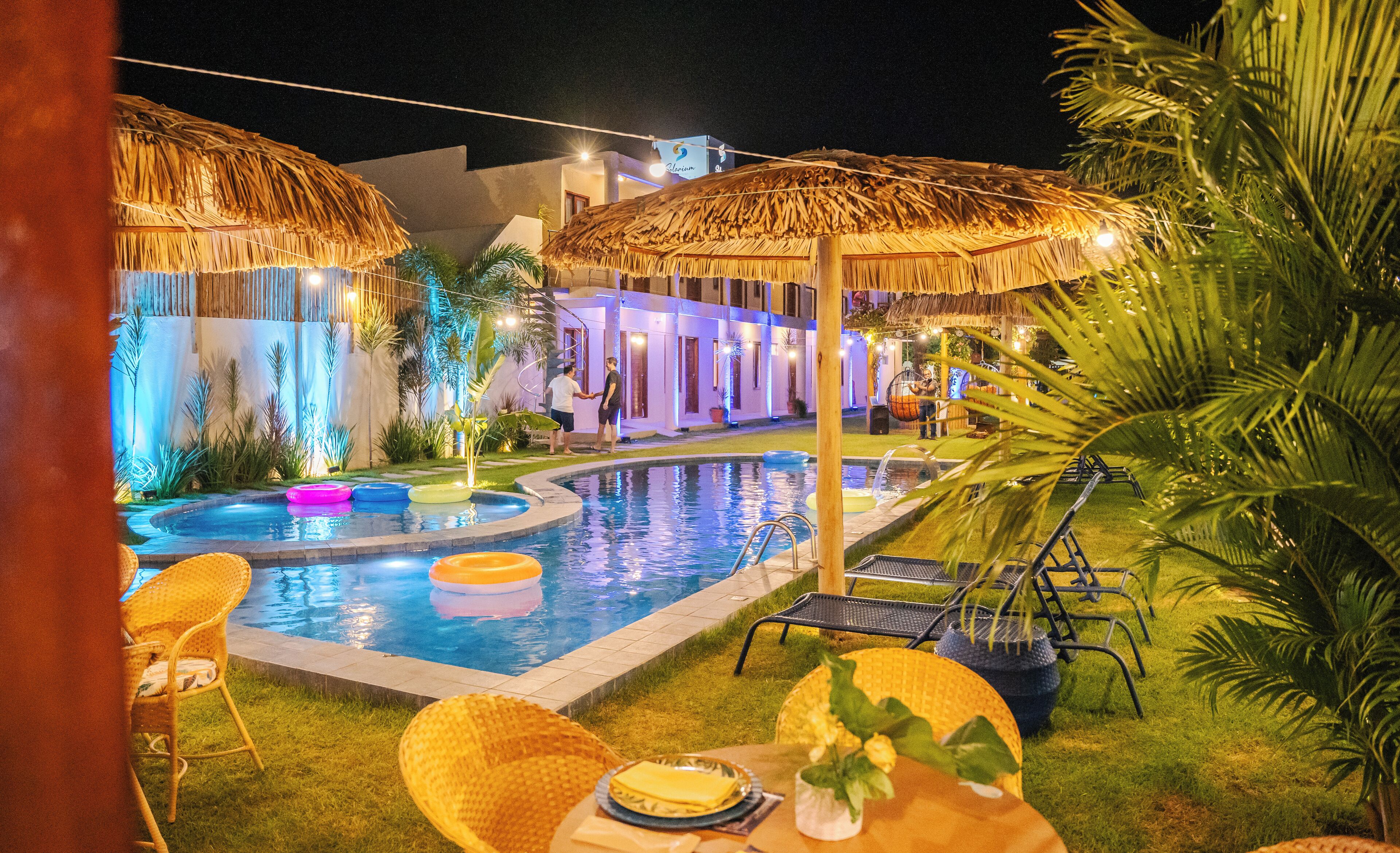 A pool area with thatched umbrellas, lounge chairs, and a dining setup with plates and cutlery.