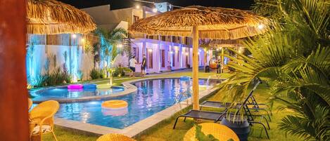 A pool area with thatched umbrellas, lounge chairs, and a dining setup with plates and cutlery.