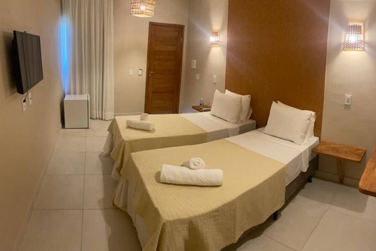 Ein Hotelzimmer mit zwei Betten, einem Fernseher, einem kleinen Tisch und einer Wandleuchte.