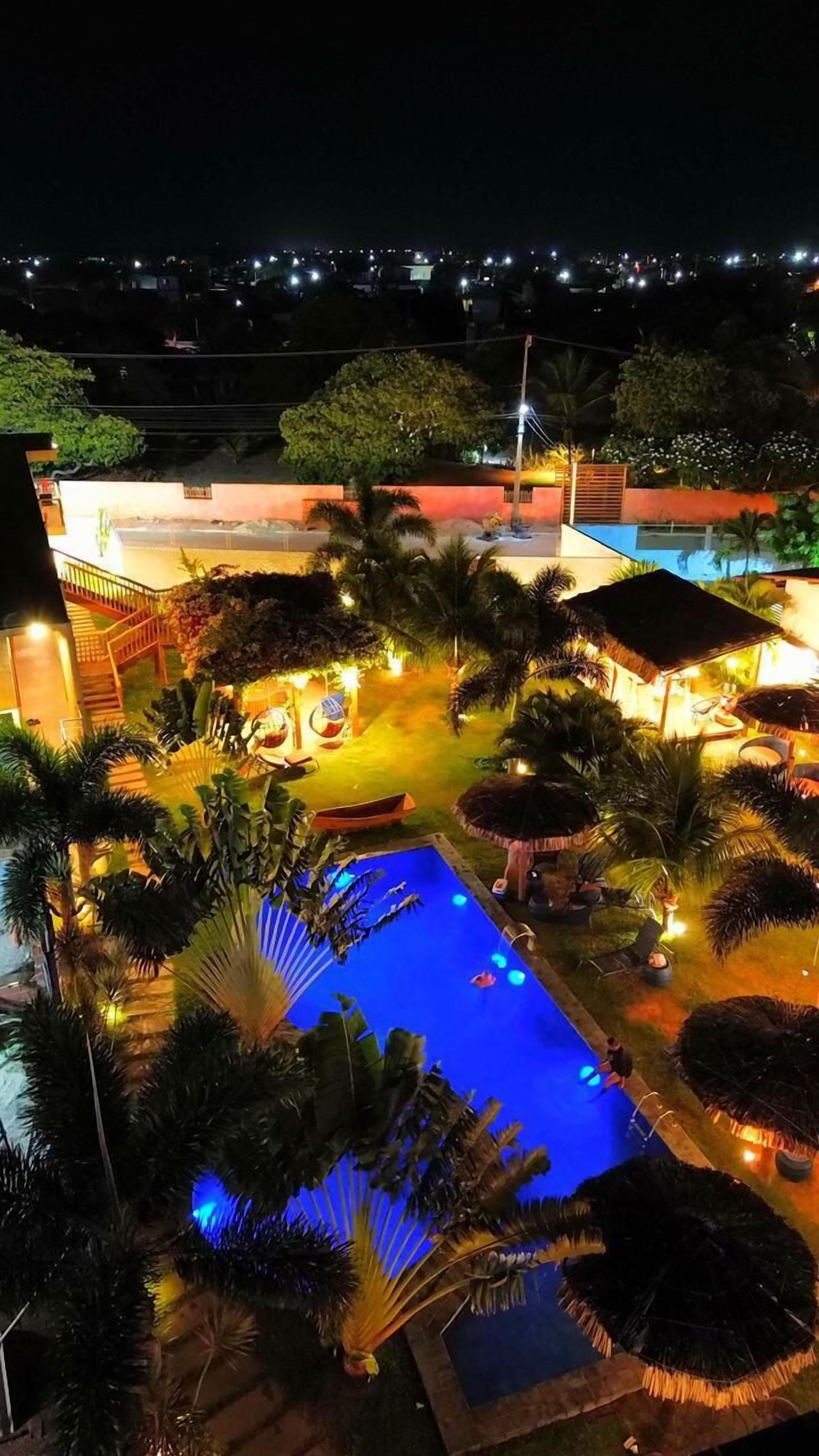 A nighttime view of a resort with a swimming pool, palm trees, and a well-lit lounge area.