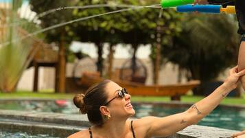 A person in a pool with a clear sky and greenery in the background.