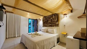 A bedroom with a bed, a small table, a refrigerator, and a wall with a geometric pattern.
