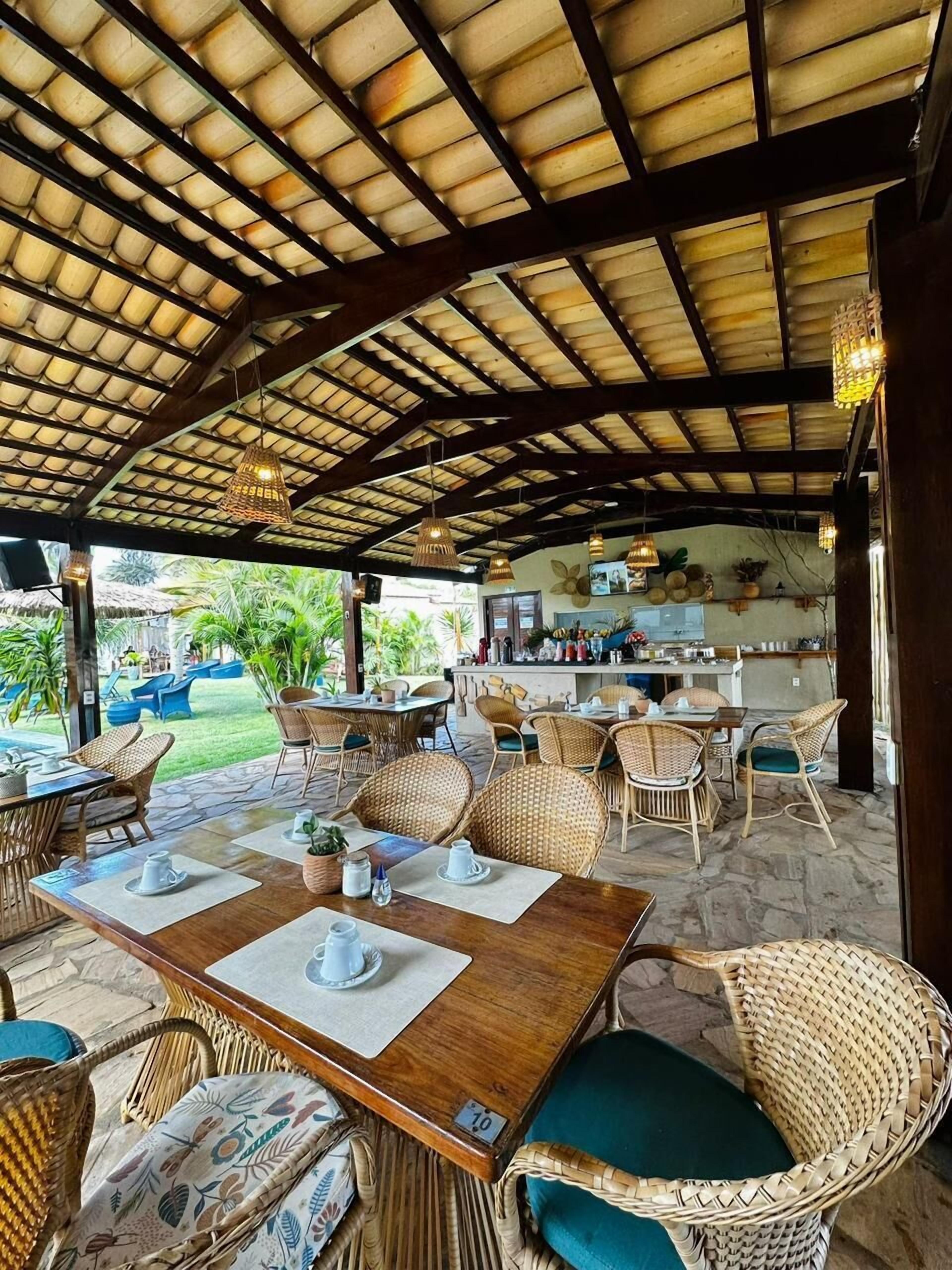 An outdoor dining area with wicker furniture, a covered roof, and a kitchen in the background.