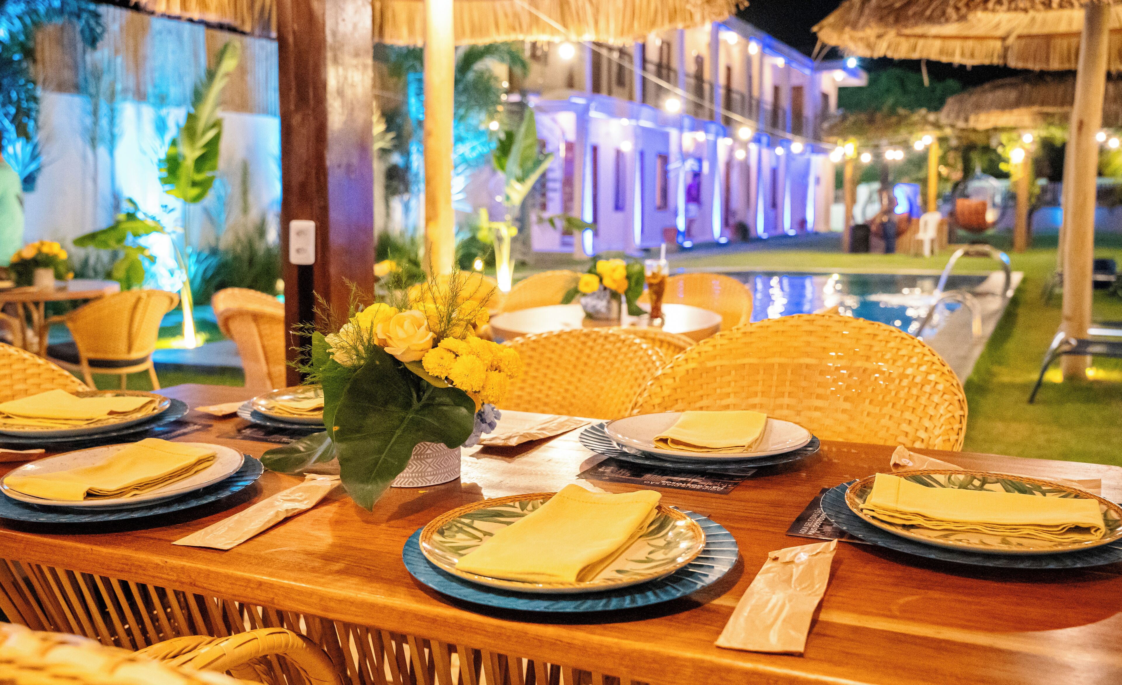 Una mesa de comedor dispuesta con platos, servilletas y un jarrón de flores amarillas.