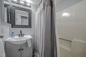Une salle de bain avec un lavabo blanc, un miroir, une serviette et un rideau de douche.
