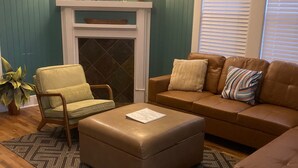 Ein Wohnzimmer mit türkisfarbenen Wänden, einem Kamin, einem braunen Ledersitzhocker, einer braunen Ledersofa und einem grünen Sessel.