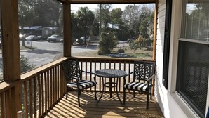 Eine überdachte Veranda mit Holzdeck, zwei Stühlen und einem kleinen Tisch.