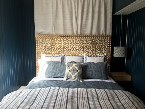 A bed with a patterned headboard, a striped bedspread, and several pillows.