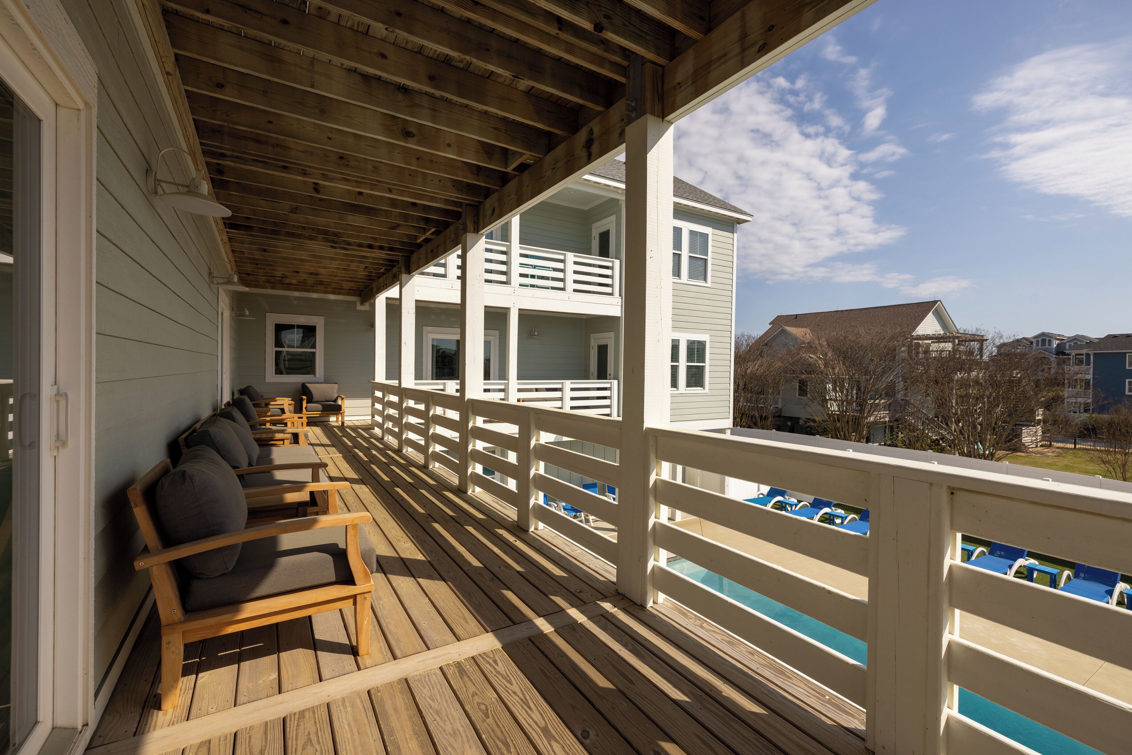 A wooden deck with outdoor seating, a white railing, and a view of a building with multiple windows.