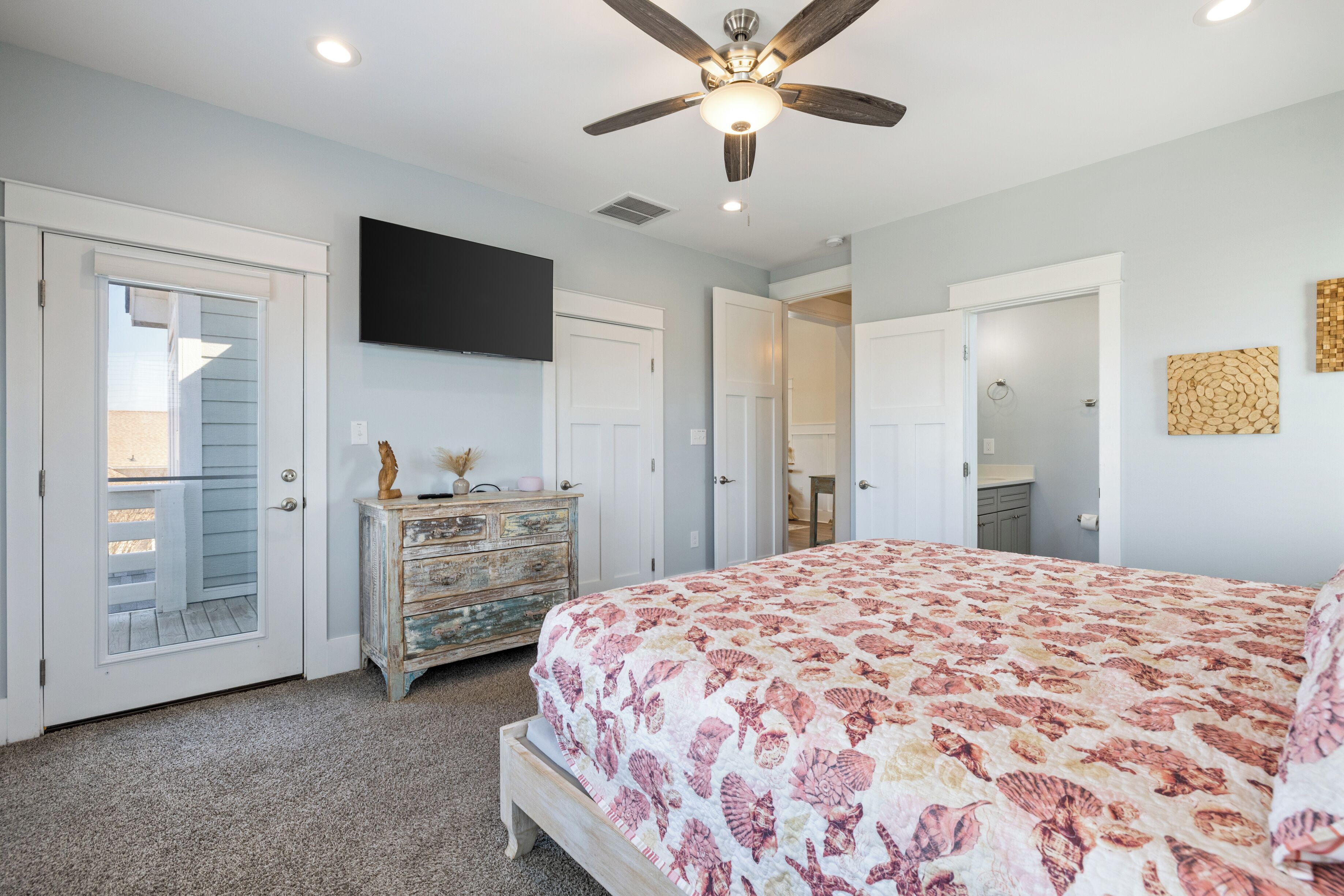 A bedroom with a bed, dresser, ceiling fan, and a TV on the wall.