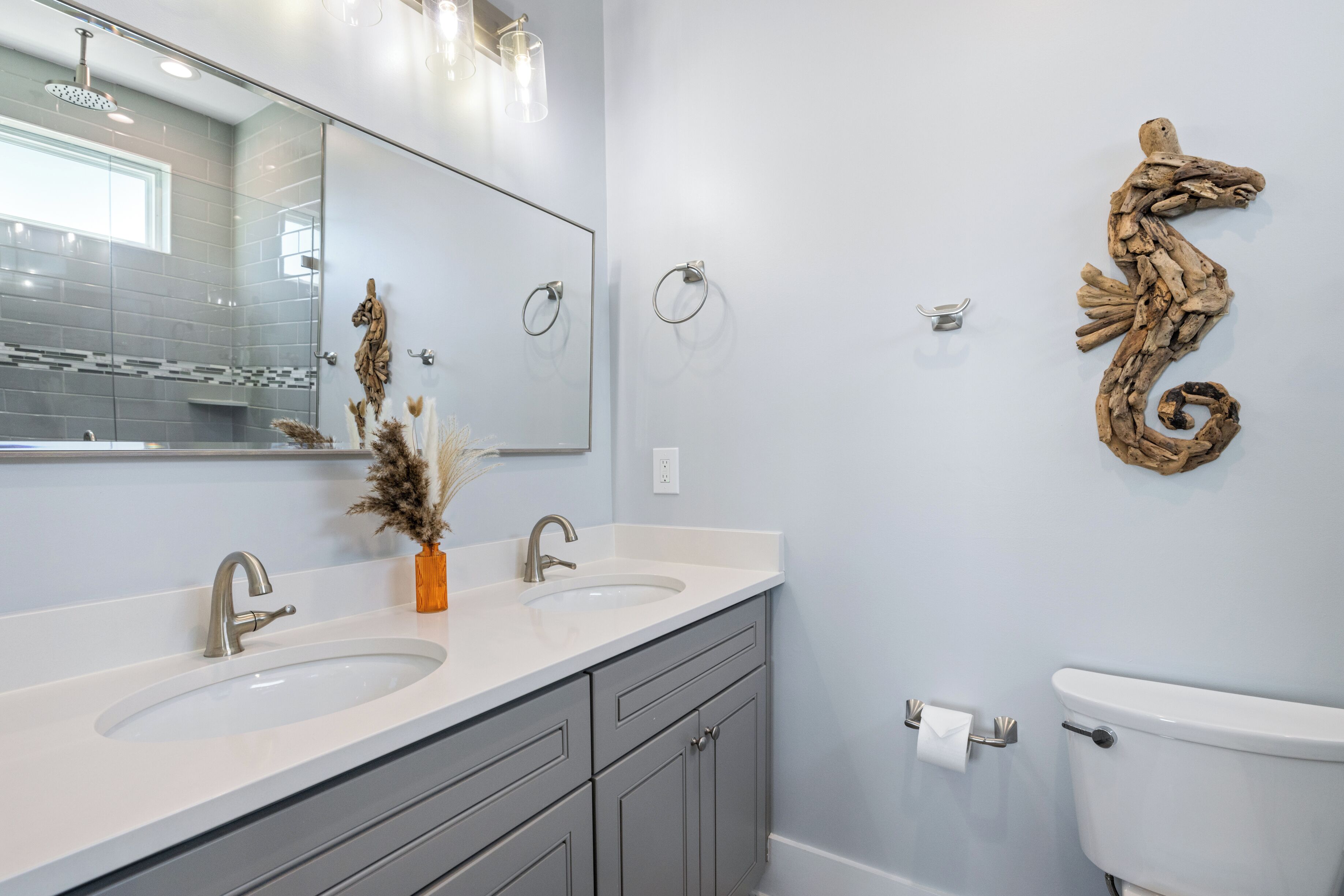 A bathroom with two sinks, a mirror, a toilet, and a decorative seahorse on the wall.
