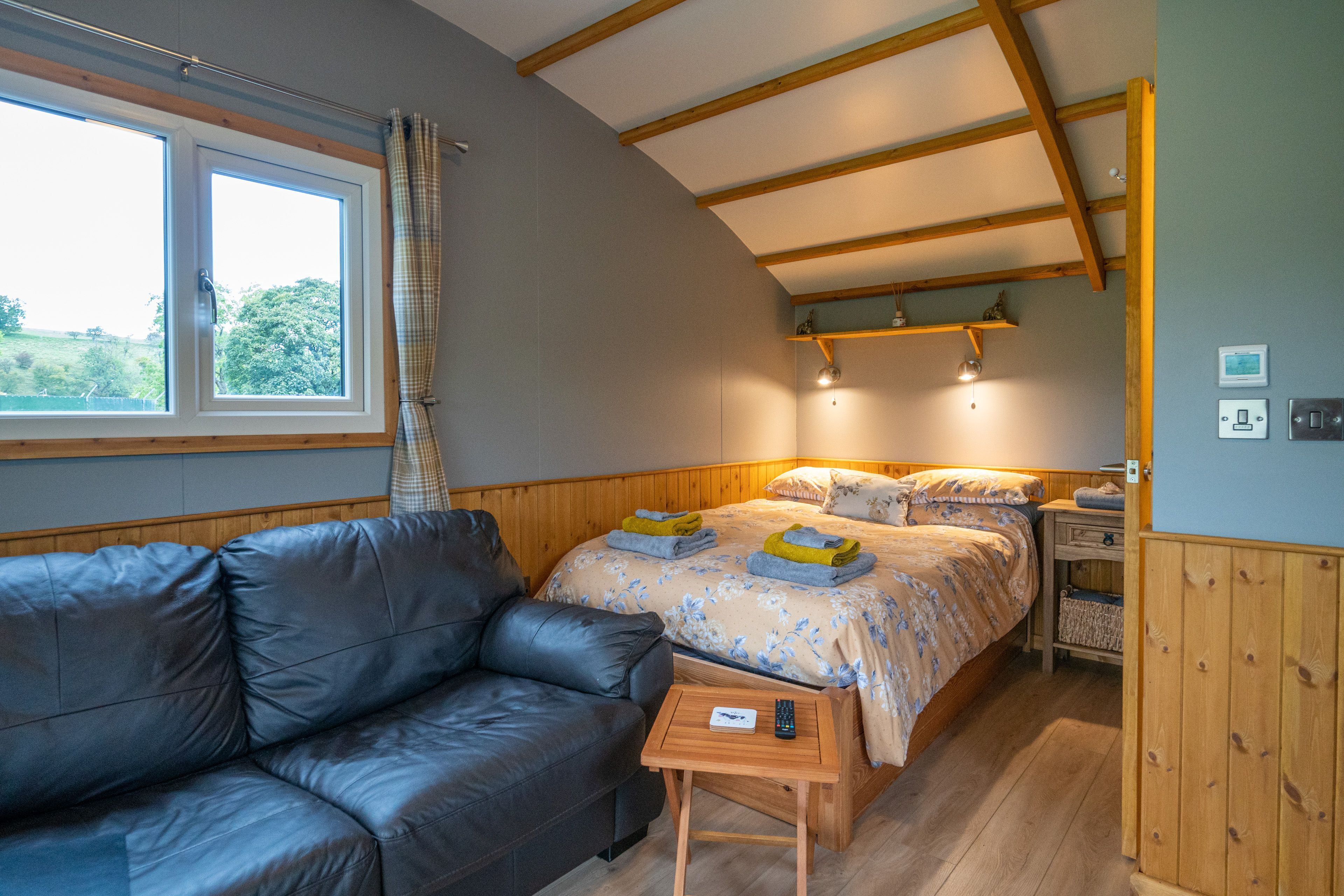 A cozy room with a bed, a leather sofa, a small wooden table, and a window with curtains.