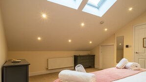 Ein Schlafzimmer mit Oberlicht, einem Bett mit rosa Bettdecke, einem Schminktisch und einer Heizung.