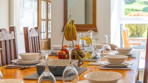 Une table à manger dressée avec de l’assiette blanche, des bols et un panier de fruits.