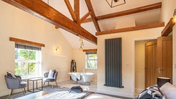 Une chambre à coucher avec un grand lit, deux fauteuils, une baignoire et des poutres en bois au plafond.