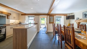 Une cuisine moderne avec des poutres en bois, un îlot central et un coin repas comprenant des chaises et une table en bois.