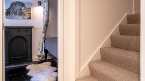 A staircase with beige carpeted steps, a dark wooden door, and a white fluffy rug on the floor. - Low Nook Cottage -  Newly refurbished cottage for three guests (Broughton-in-Furness)