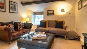 A living room with a brown leather sofa, a grey sofa, and a grey ottoman. There are framed pictures on the walls and a lamp on a side table. - Low Nook Cottage -  Newly refurbished cottage for three guests (Broughton-in-Furness)