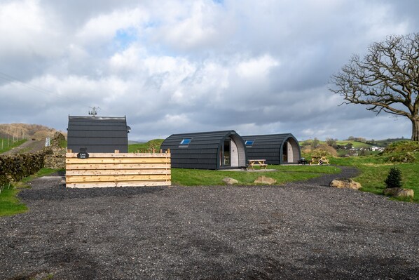 A modern, rustic building with a large wooden structure in the foreground and two dome-shaped cabins in the background. - Hen House - Family-friendly glamping pod on a working farm (Underbarrow)