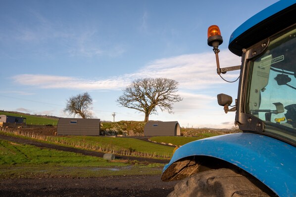 A blue tractor with a cabin and a mounted orange light, set against a rural landscape with green fields and a clear sky.