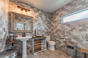 Een badkamer met een stenen muur, een wit wastafelmeubel, een toilet en een houten kast.