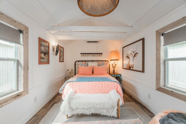 Een slaapkamer met een bed, een zachte witte bank, een vloerkleed en lijstwerken aan de wanden.